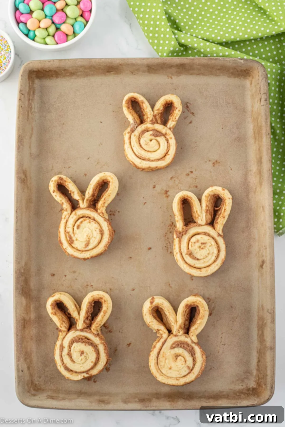 Hoppy Swirls 4 Unbaked cinnamon rolls carefully shaped into distinct bunny forms with two prominent ears on a baking sheet, ready for the oven.