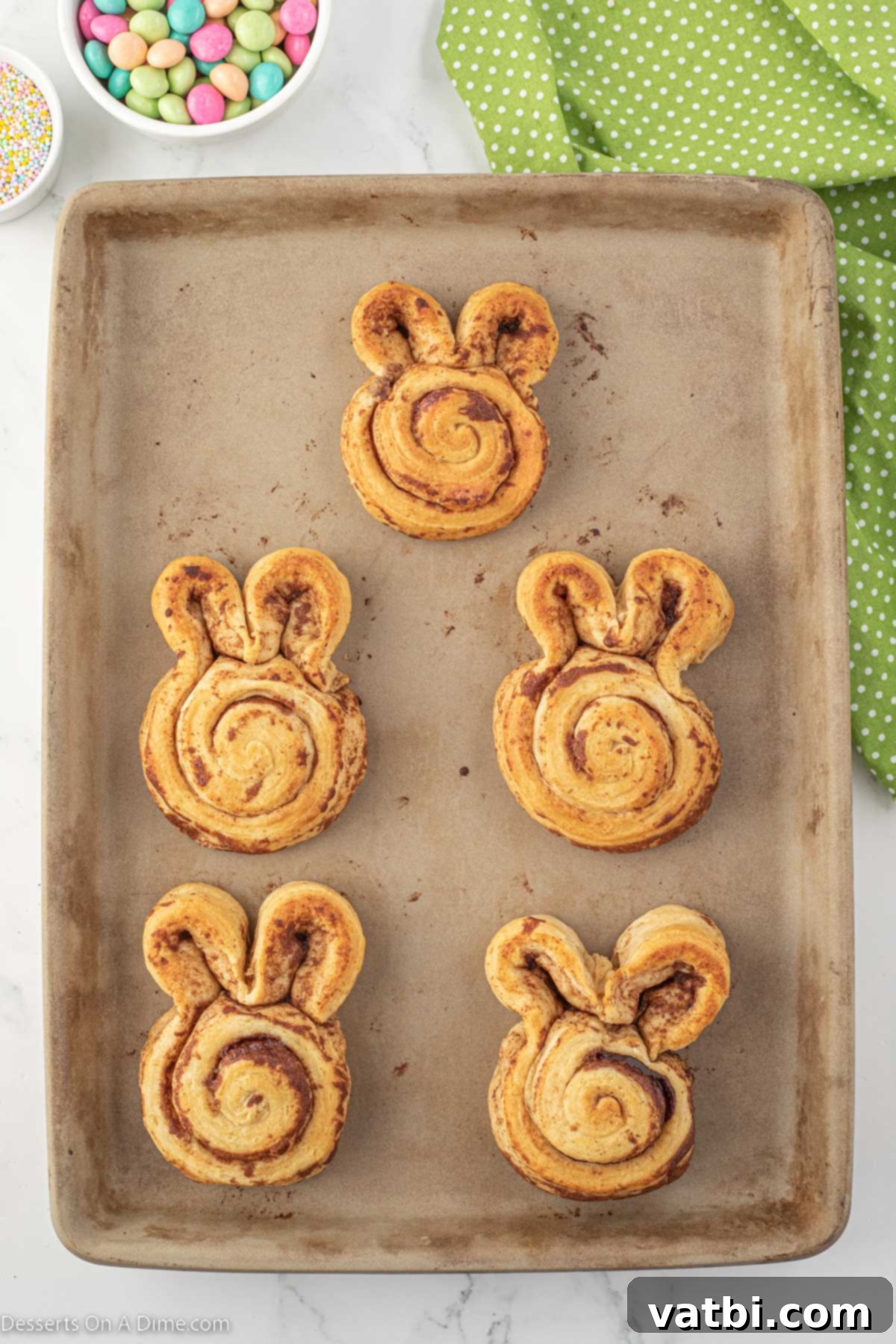 Hoppy Swirls 5 Freshly baked cinnamon rolls, still warm from the oven, maintaining their bunny shapes on a baking sheet, ready for the next step of decoration.