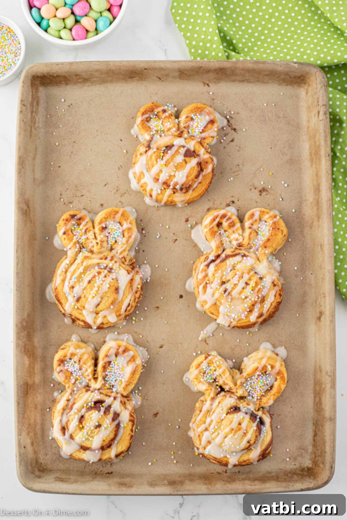 Hoppy Swirls 6 Warm, baked bunny cinnamon rolls on a baking sheet being generously drizzled with the included cream cheese icing, preparing them for festive toppings.