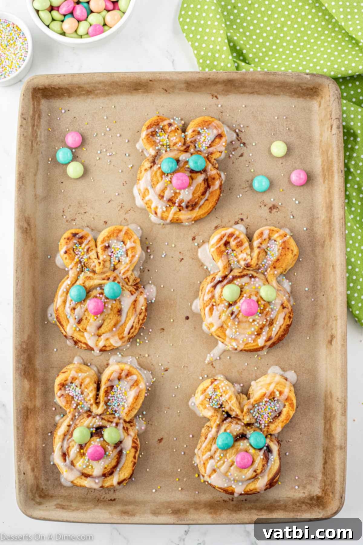 Hoppy Swirls 7 Close-up of baked bunny cinnamon rolls, now iced and adorned with colorful pastel sprinkles and M&Ms carefully placed to form charming bunny faces with eyes and a nose.