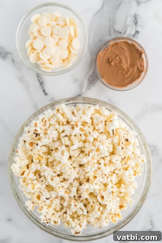 Three key ingredients for Cookie Butter Popcorn laid out: a bowl of freshly popped popcorn, a bowl of white melting chocolate, and a jar of creamy cookie butter, demonstrating the recipe's simplicity.