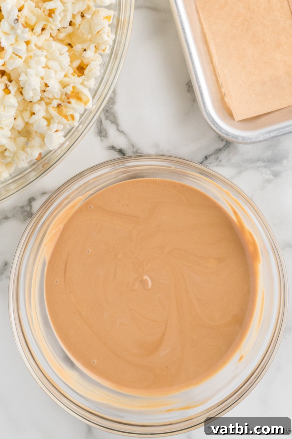 A close-up shot of the perfectly smooth and combined cookie butter and white melting chocolate mixture in a bowl, ready for coating the popcorn.