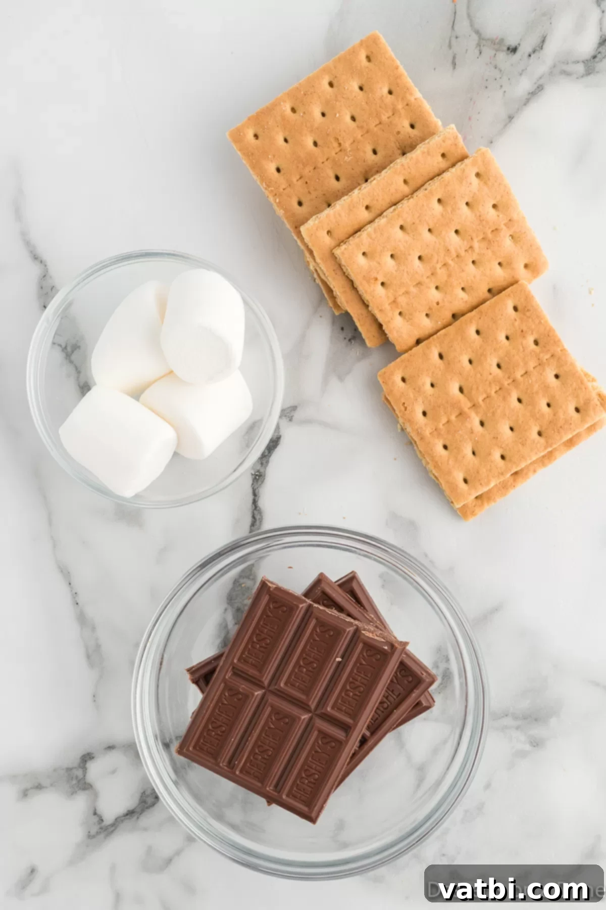Key ingredients for Air Fryer S'mores: graham crackers, large marshmallows, and milk chocolate bars, neatly arranged on a white surface.