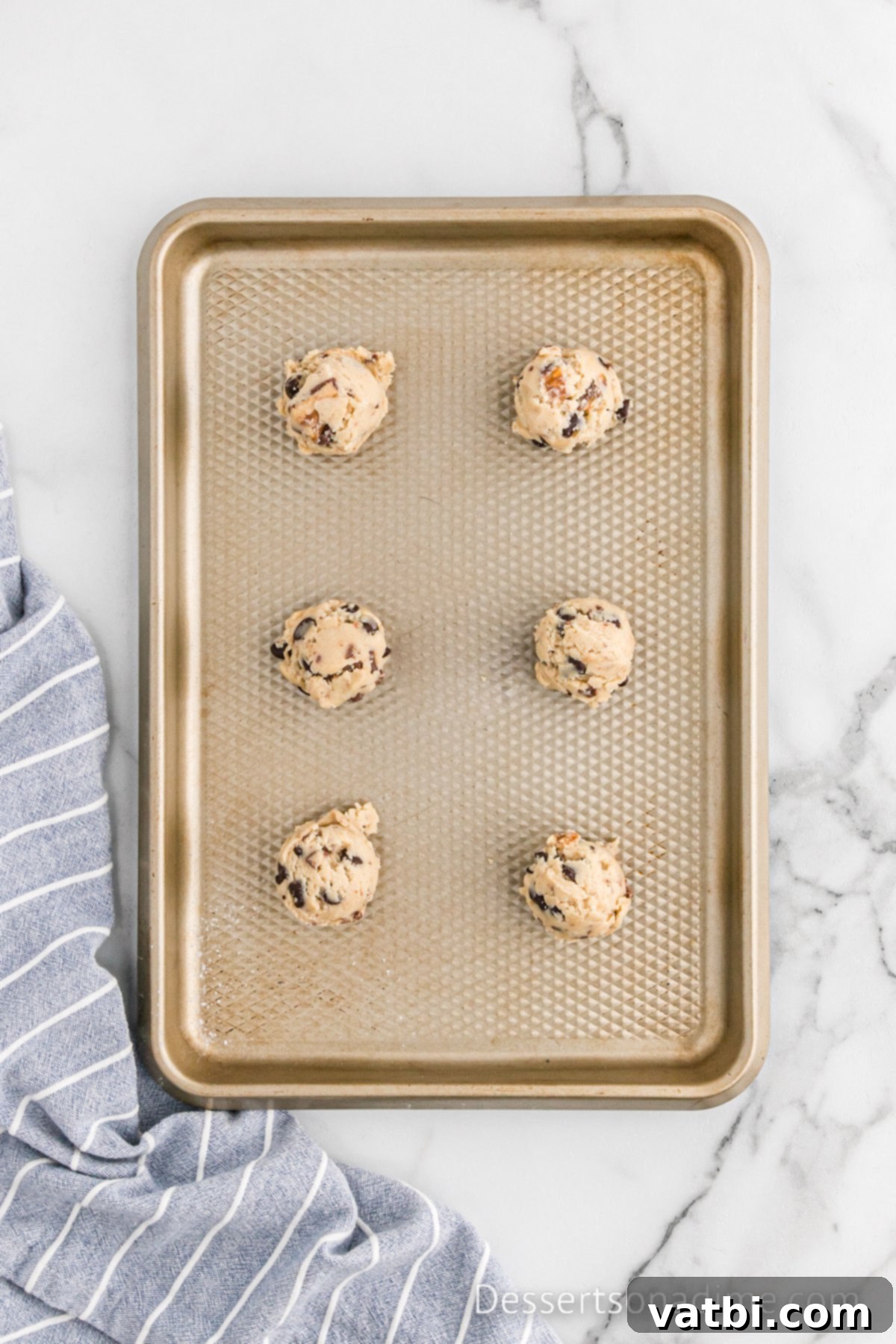Scoops of Snickers cookie dough arranged on a baking sheet lined with parchment paper.