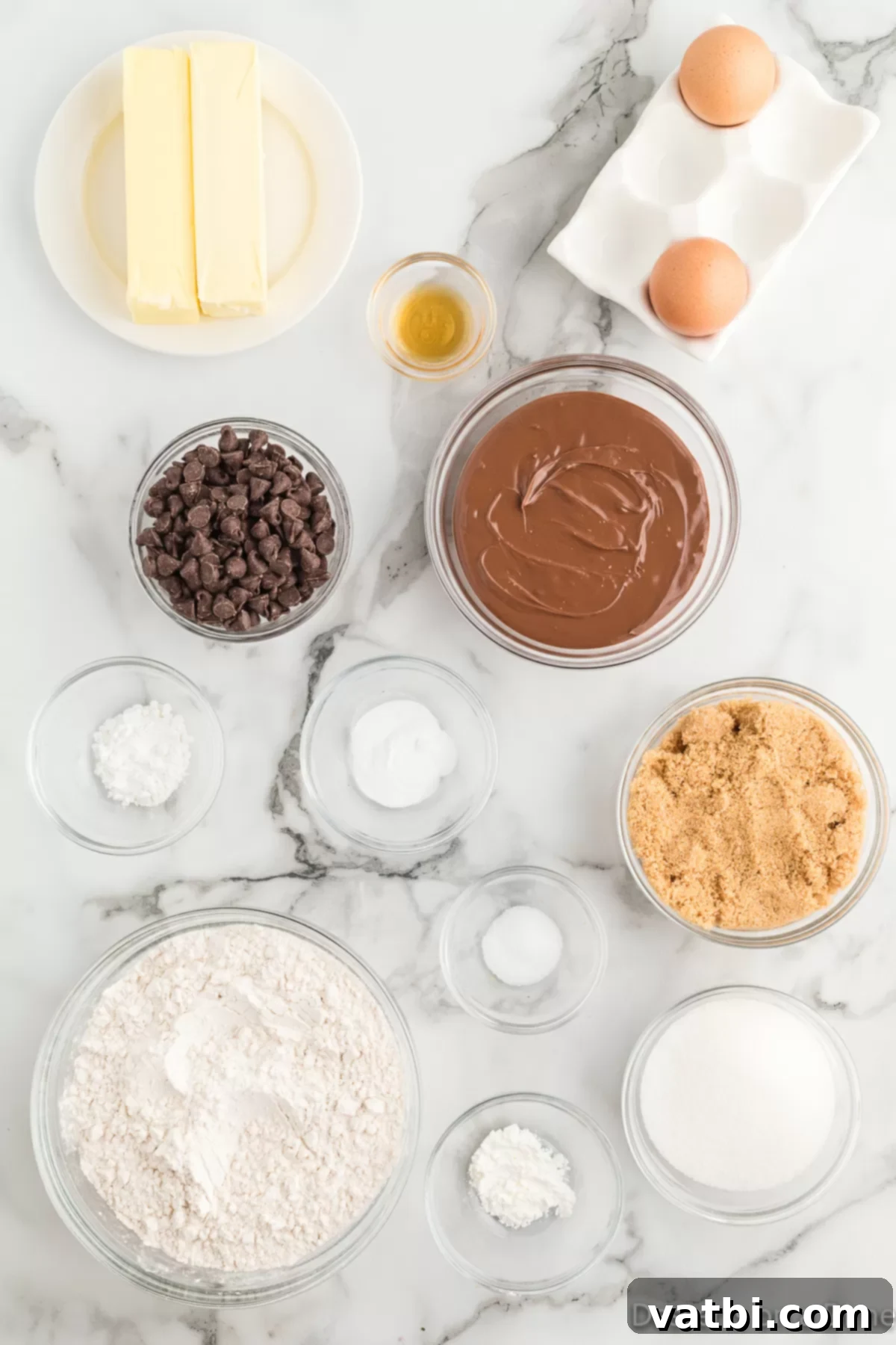 Decadent Nutella Stuffed Cookies 3 Ingredients for Nutella stuffed cookies, neatly arranged: butter, Nutella, brown sugar, eggs, vanilla extract, baking soda, flour, and chocolate chips.
