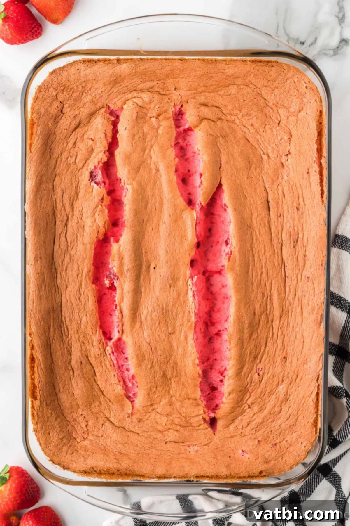 Strawberry Cloud Delight 7 Baked Strawberry Angel Food Cake cooling on a rack, with a golden brown top.