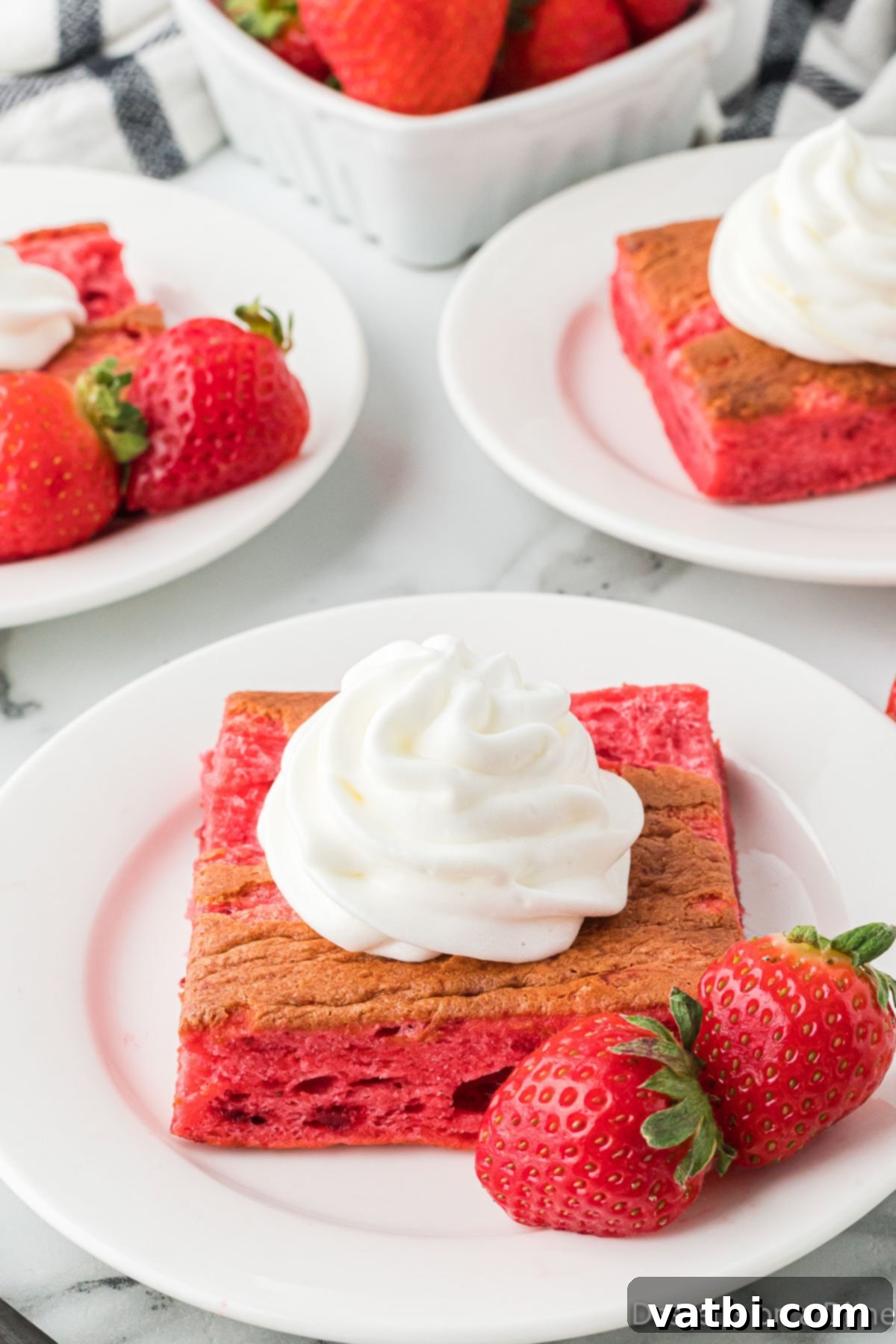 Strawberry Cloud Delight 8 A slice of Strawberry Angel Food Cake on a plate, generously topped with whipped cream and a fresh strawberry.