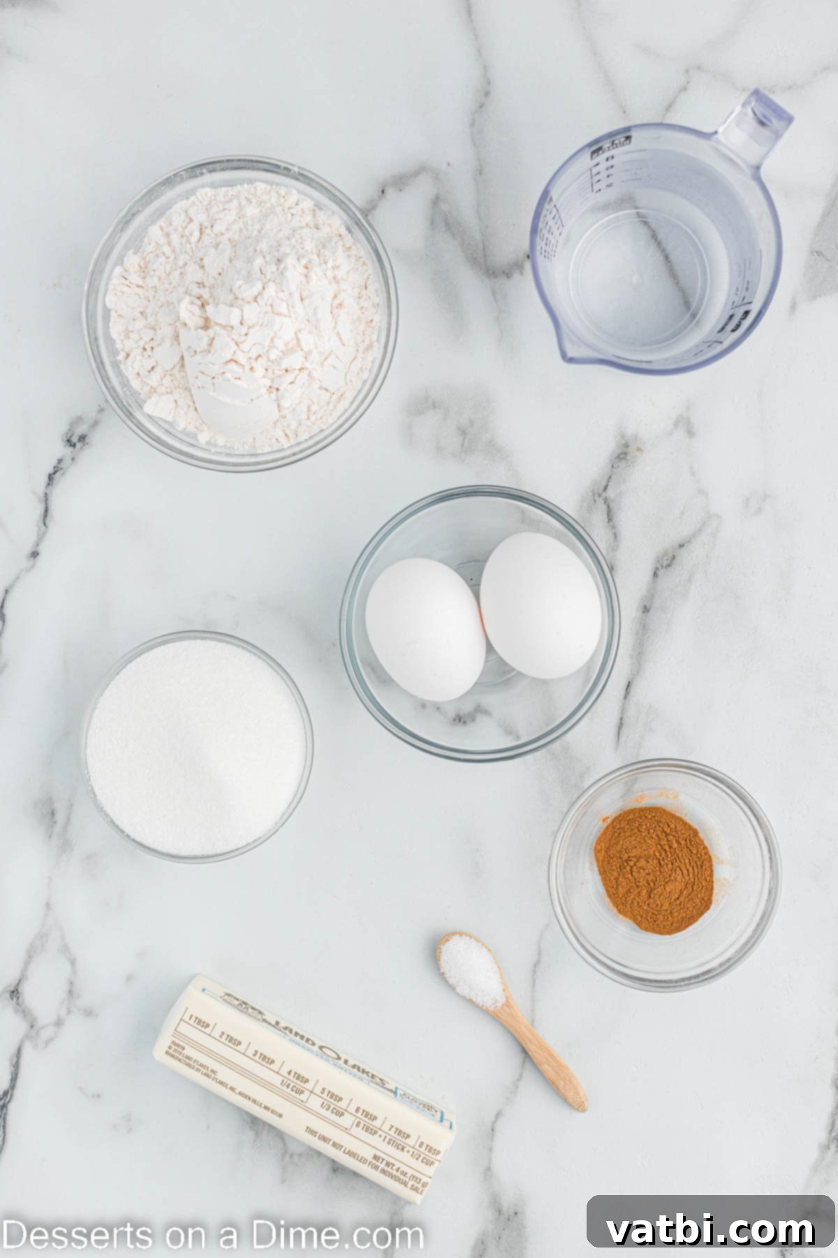 Crispy Air Fryer Churros 3 A selection of key ingredients for Air Fryer Churros, including a stick of butter, a bowl of all-purpose flour, ground cinnamon, fresh eggs, and granulated sugar.