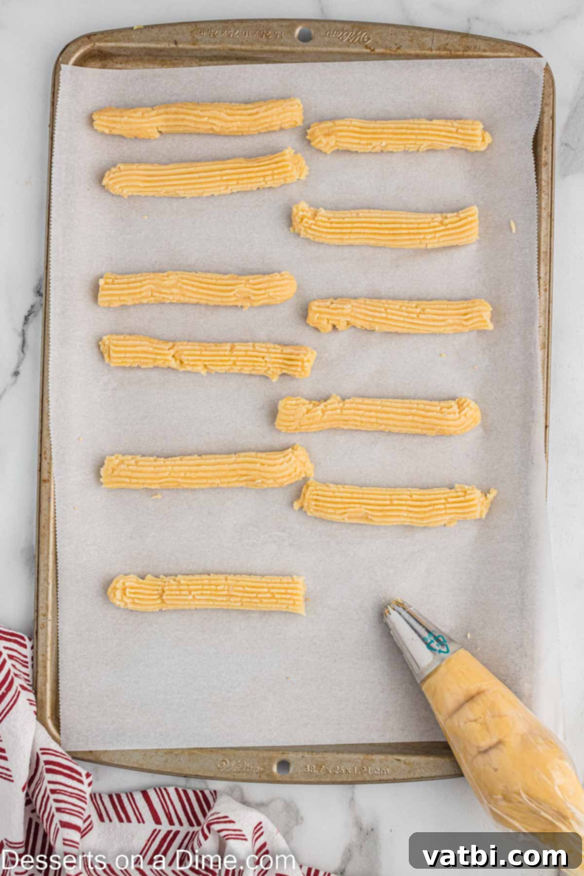 Crispy Air Fryer Churros 8 Churro dough being piped into uniform strips onto a parchment-lined baking sheet, ready for freezing.