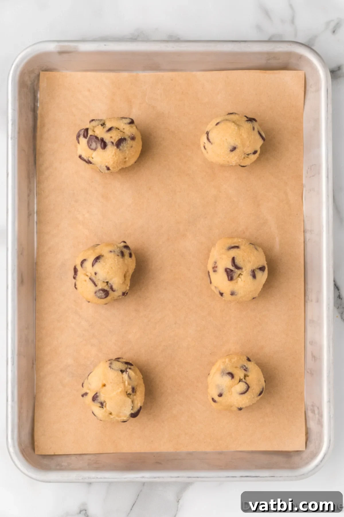 Mrs. Fields' Legendary Chocolate Chip Cookies 8 Scooped cookie dough balls evenly spaced on a baking sheet lined with parchment paper.