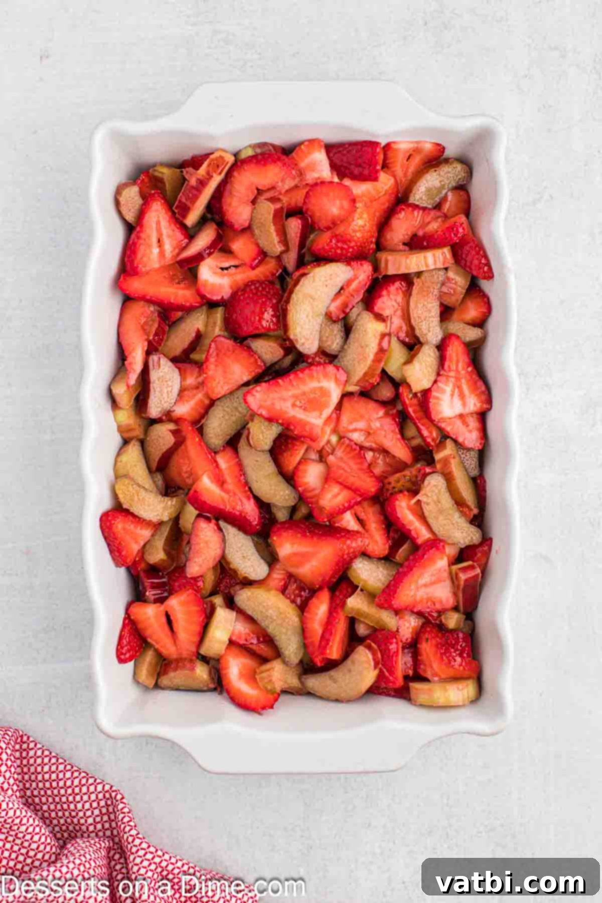 Sun-Kissed Strawberry Rhubarb Cobbler 7 The vibrant red and green strawberry rhubarb fruit filling evenly spread into the bottom of a 9x13 inch glass baking dish, ready for the topping.
