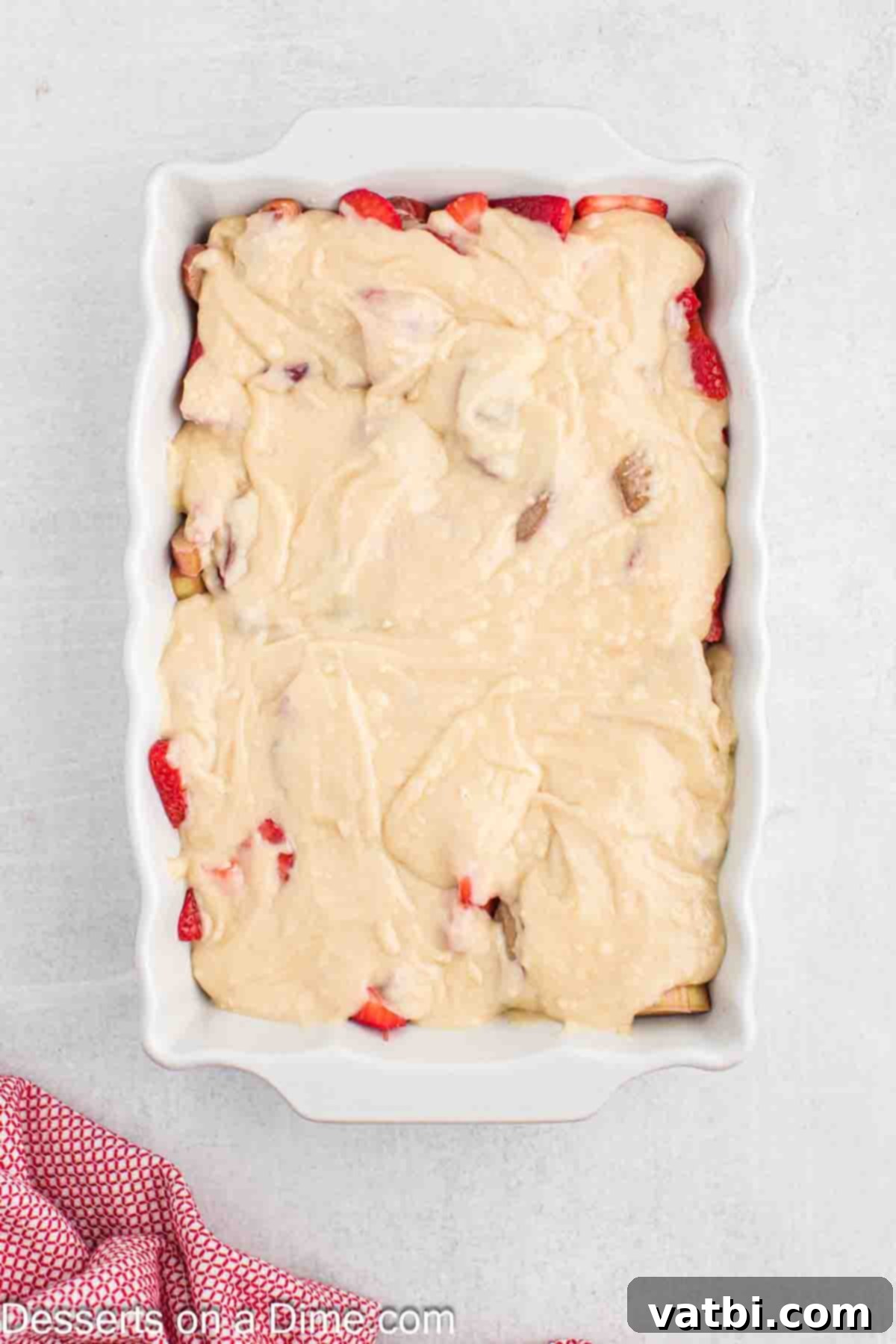 Sun-Kissed Strawberry Rhubarb Cobbler 8 The cobbler batter delicately spooned and spread over the vibrant fruit filling in the baking dish, creating an even top layer before baking.