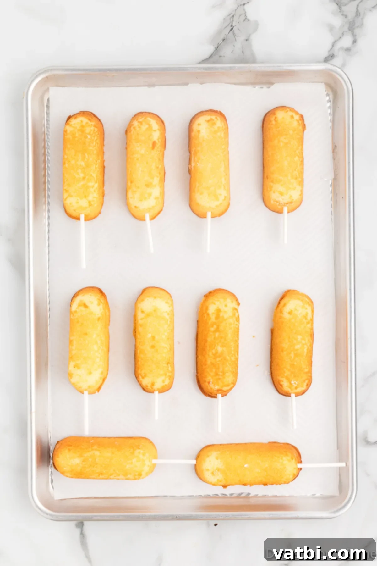 Irresistible Chocolate Glazed Twinkies 4 Twinkies with sticks inserted and placed on baking sheet.