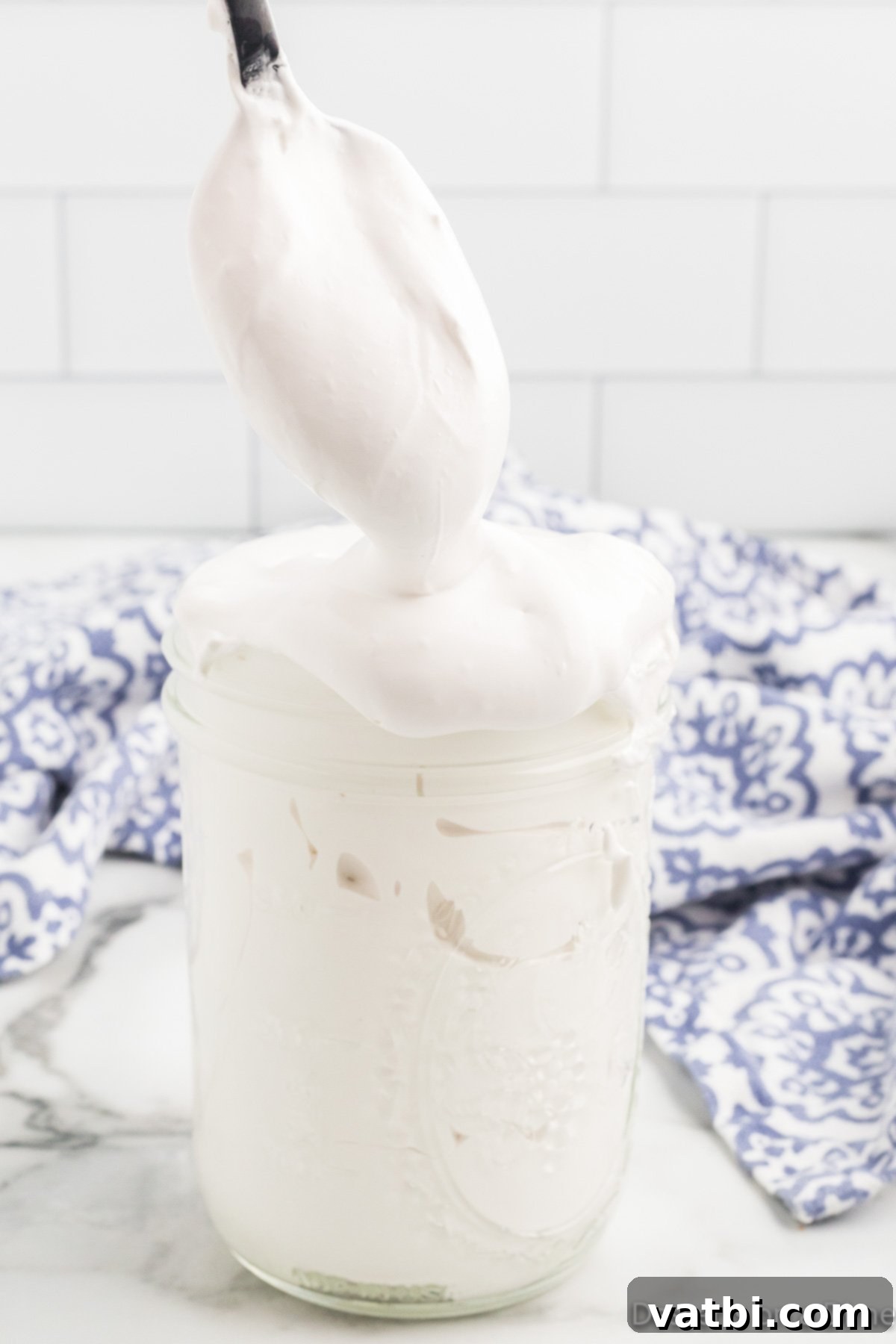A spoon dipping into a jar of delicious homemade marshmallow fluff. Give this easy recipe a try. A spoon dipping into a glass jar filled with luscious homemade marshmallow fluff, ready to be enjoyed.