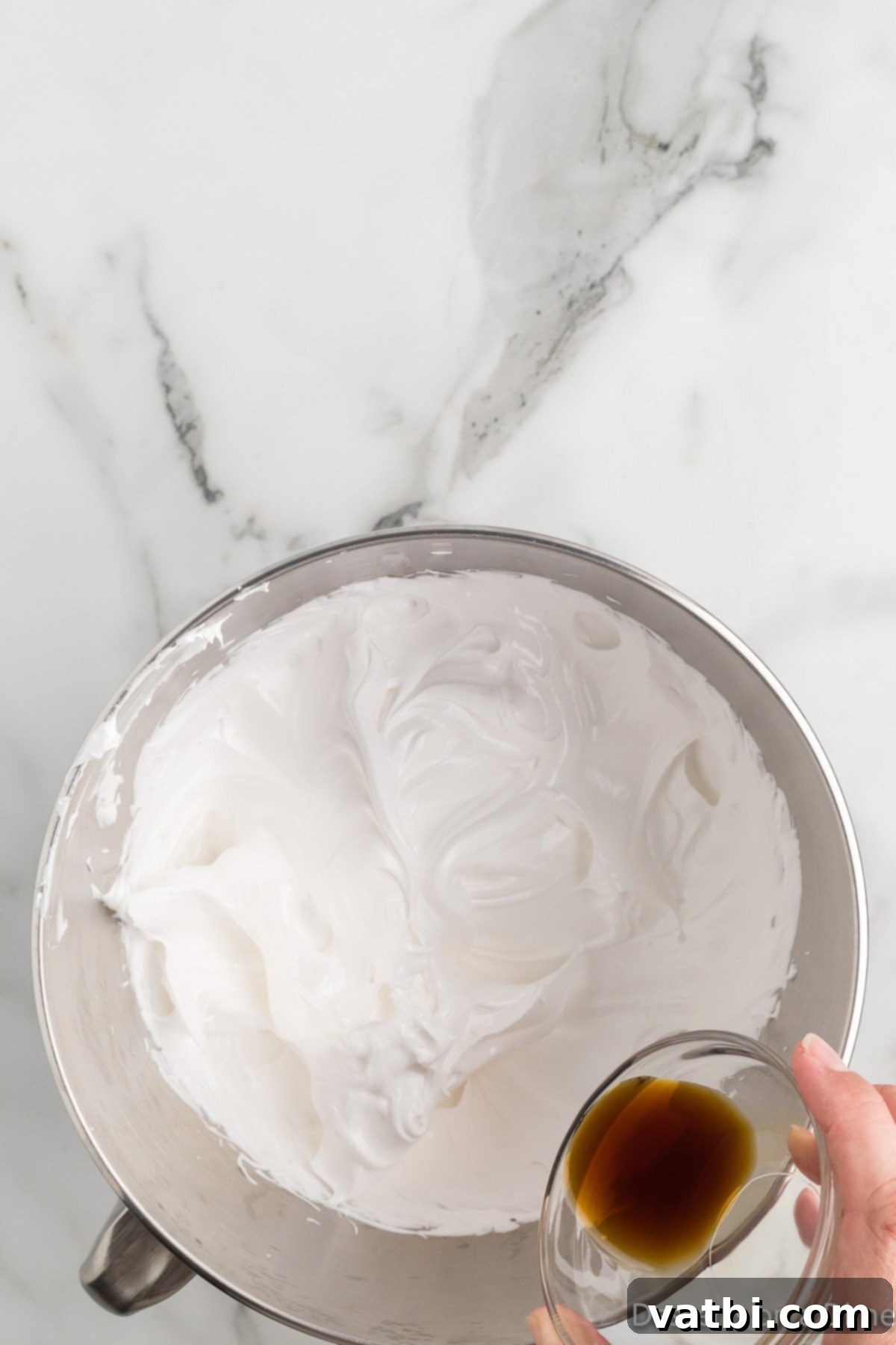 Cloud-Soft Homemade Marshmallow Fluff 7 Vanilla extract being poured into the thick, glossy marshmallow fluff in a stand mixer during the final stages of whipping.
