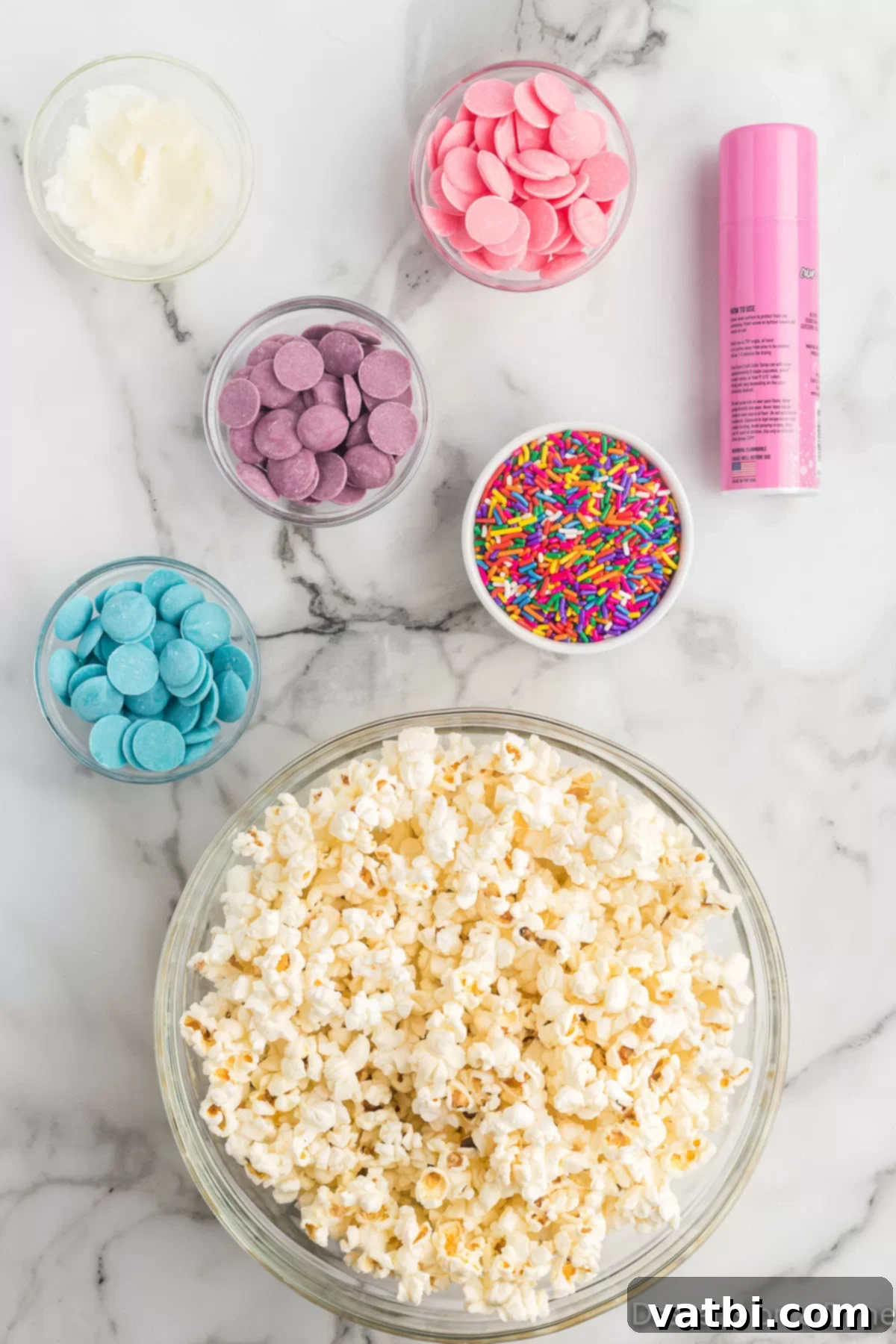 Rainbow Unicorn Popcorn 3 Ingredients for Unicorn Popcorn including popped popcorn, pink candy spray, various colored candy melts, and rainbow sprinkles.