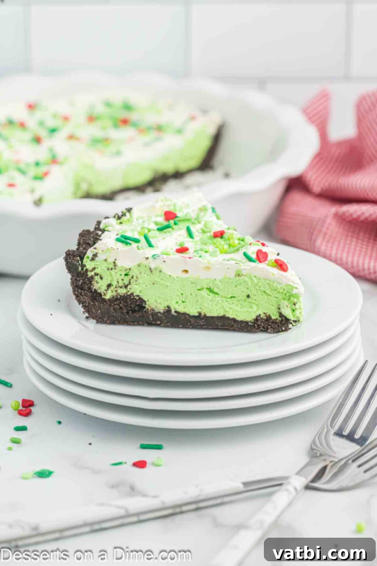 The Grinch's Heart-Melting Holiday Pie 2 A vibrant green slice of No-Bake Grinch Pie with red and green sprinkles on a white plate, ready to be enjoyed.
