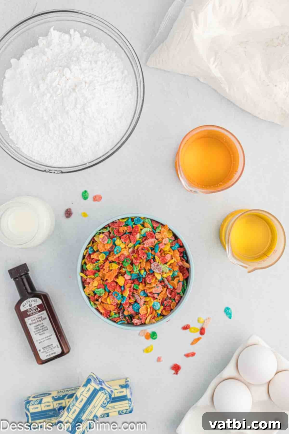 Rainbow Cereal Cupcakes 3 Ingredients laid out for making Fruity Pebbles cupcakes: a box of white cake mix, eggs, a bowl of Fruity Pebbles cereal, softened butter, and powdered sugar.