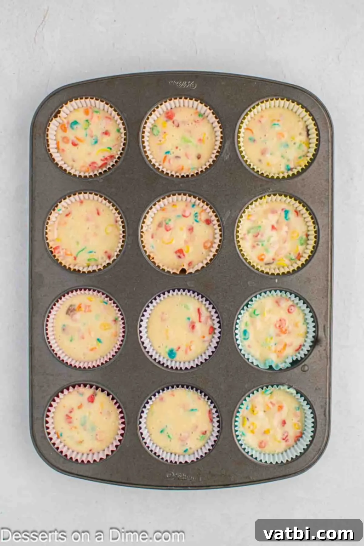 Rainbow Cereal Cupcakes 6 Cupcake liners filled three-quarters full with Fruity Pebbles batter in a muffin tin.