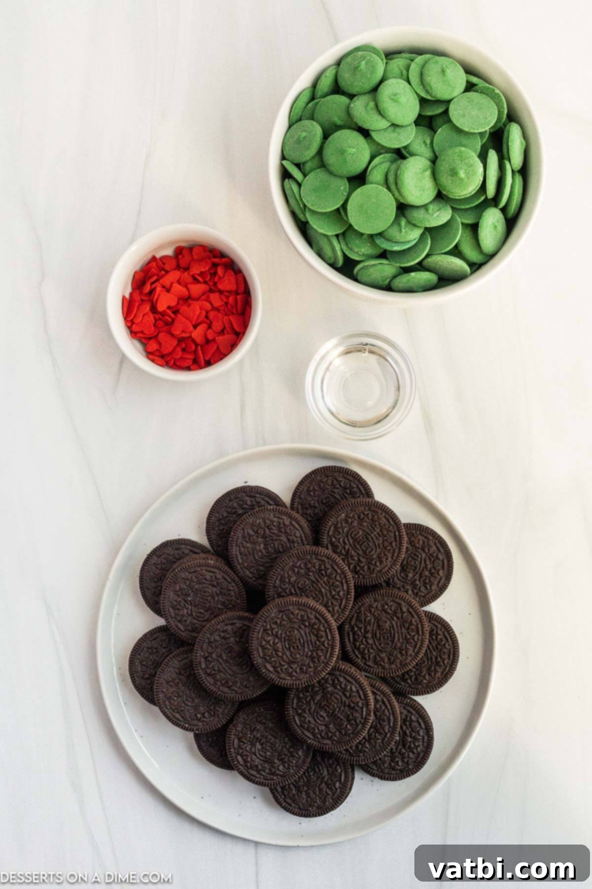 Collection of ingredients for Grinch Oreos, including Oreos, green candy melts, coconut oil, and red heart sprinkles.