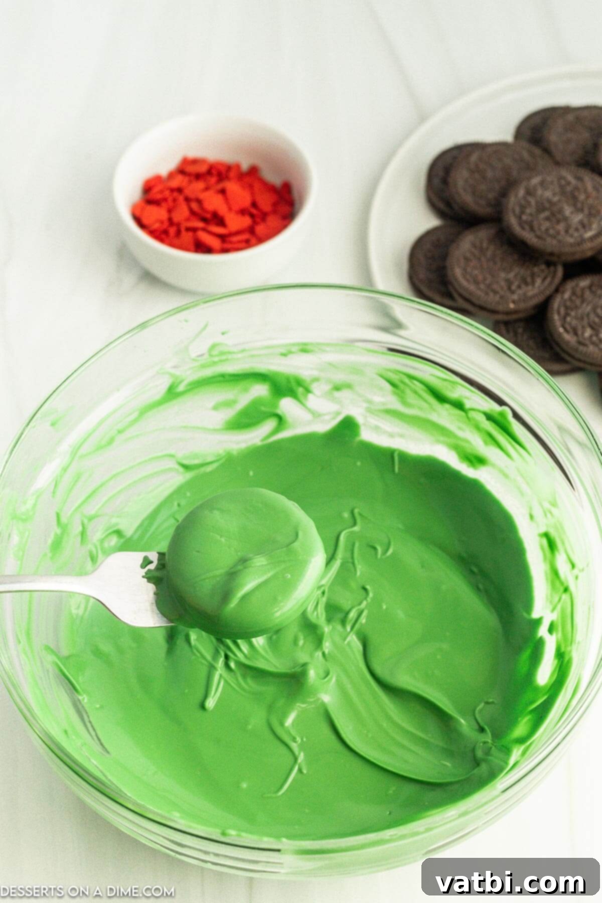 An Oreo cookie being dipped into melted green candy coating with a fork.