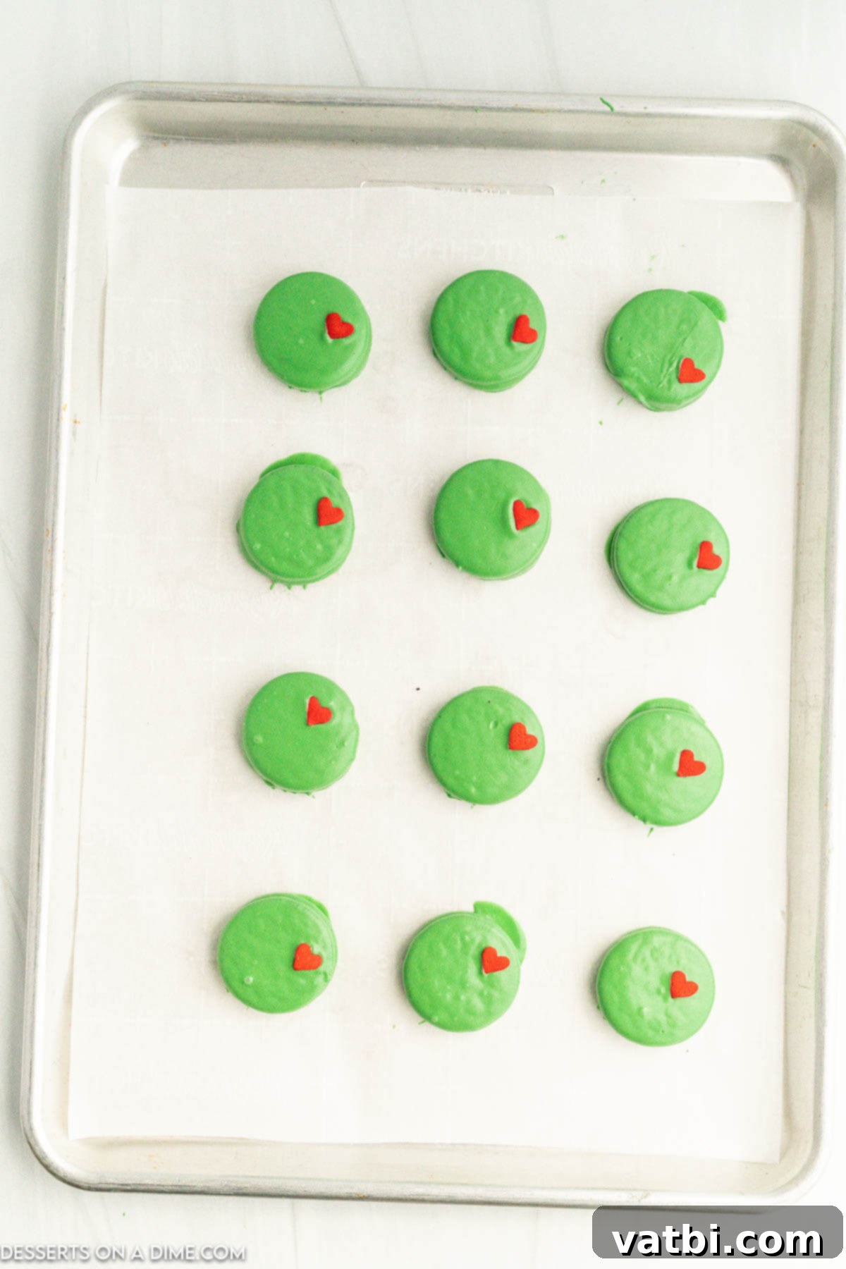 Several green-coated Oreo cookies arranged on a baking sheet lined with parchment paper.