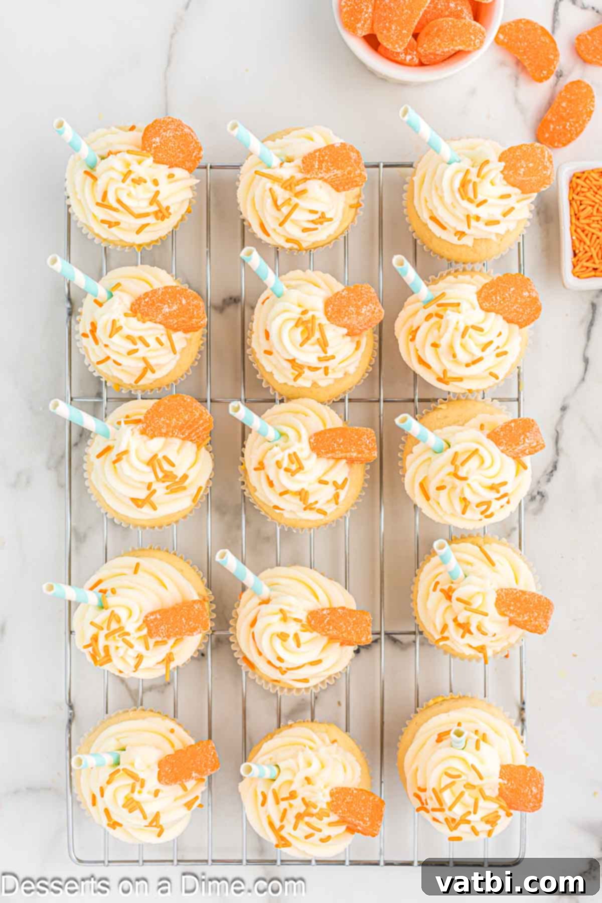 Velvet Orange Dream Cupcakes 11 Finished orange creamsicle cupcakes topped with frosting, orange jimmies, and candied orange slices on a wire rack.