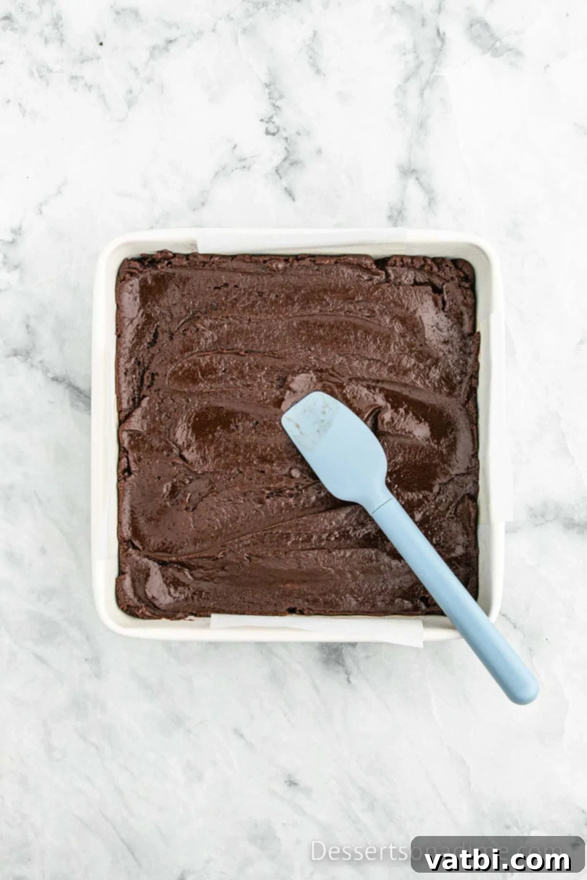 Chocolate fudge mixture spread evenly in a parchment-lined baking dish.