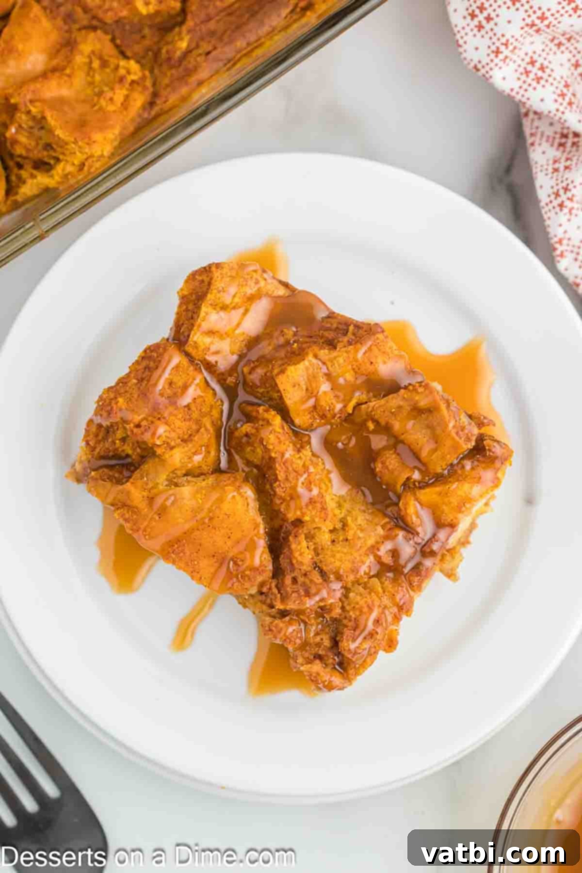 Decadent Pumpkin Bread Pudding 13 A baked pumpkin bread pudding in a dish, with a serving removed to a plate, ready for enjoyment