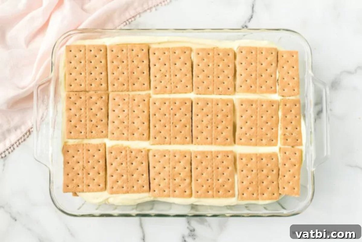 Effortless No-Bake Eclair Cake 5 Topping the pudding with graham crackers in a baking dish.