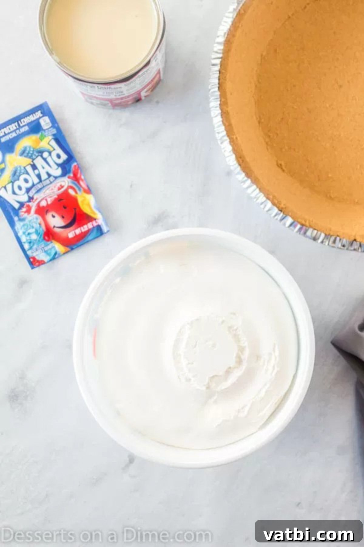Kool Aid Pie Ingredients: Graham Cracker Crust, Sweetened Condensed Milk, Cool Whip, and Kool-Aid Mix Close-up shot of the four simple ingredients for Kool-Aid pie: a graham cracker crust, a can of sweetened condensed milk, a tub of whipped topping, and a packet of Kool-Aid mix, arranged neatly on a kitchen counter.