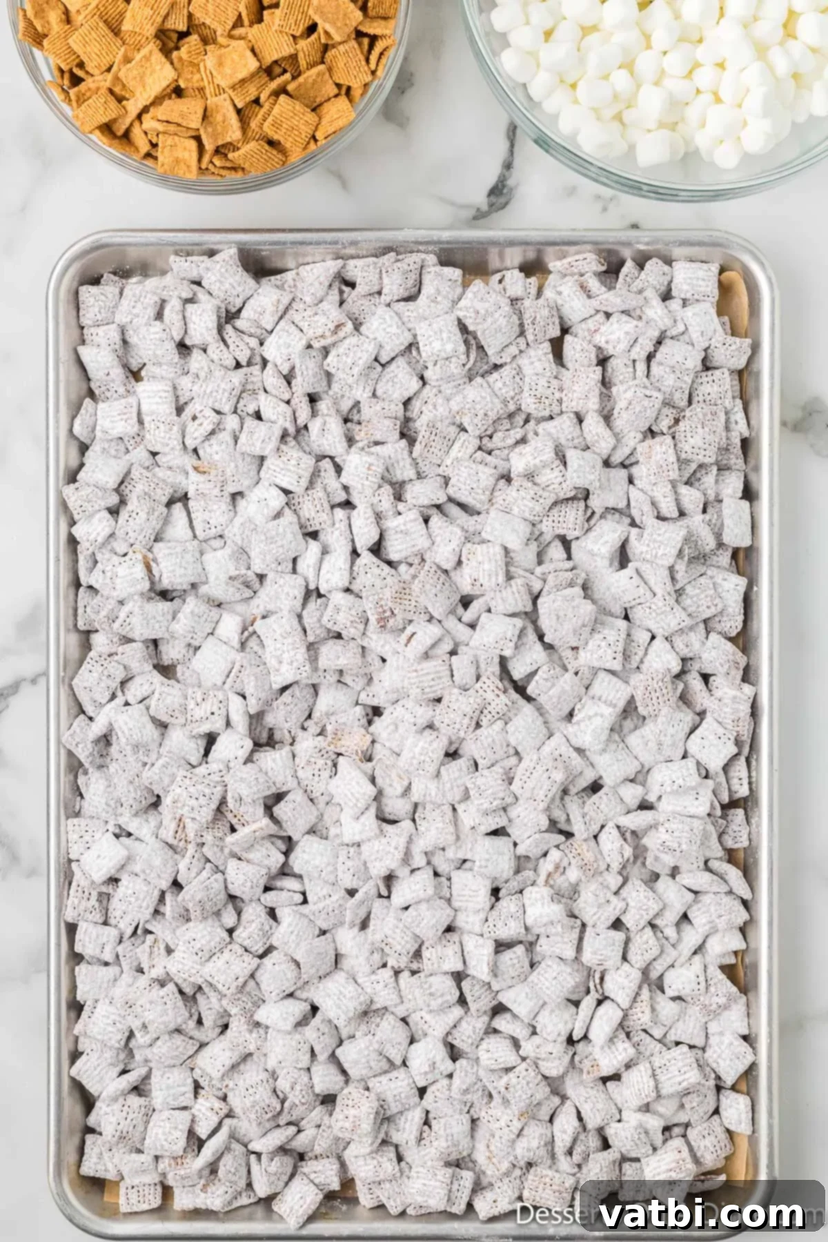 S'mores Campfire Crunch 9 Powdered sugar-coated puppy chow spread out on a baking sheet to cool.