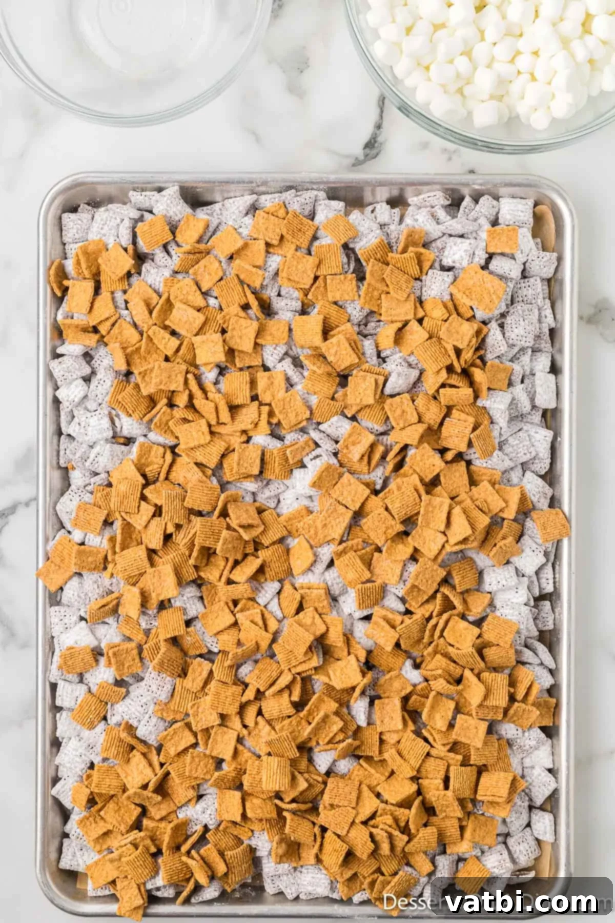 S'mores Campfire Crunch 10 Golden Grahams cereal being sprinkled over the cooled puppy chow on a baking sheet.