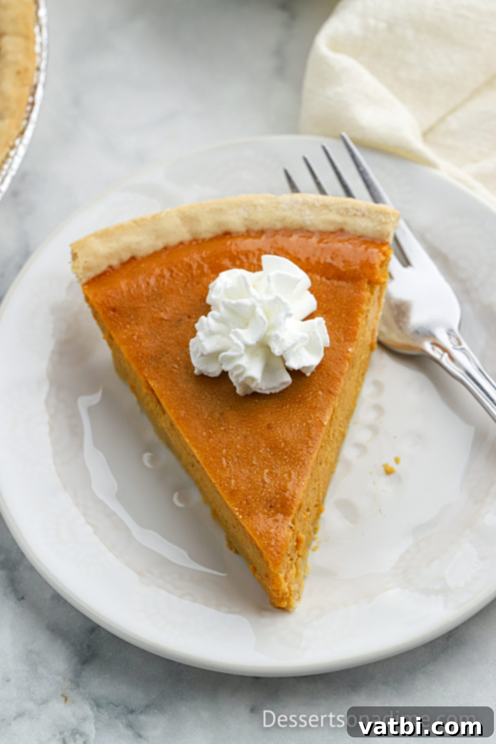 A beautifully baked slice of Eagle Brand Pumpkin Pie, topped with a generous dollop of whipped cream, on a white plate, ready to be enjoyed.