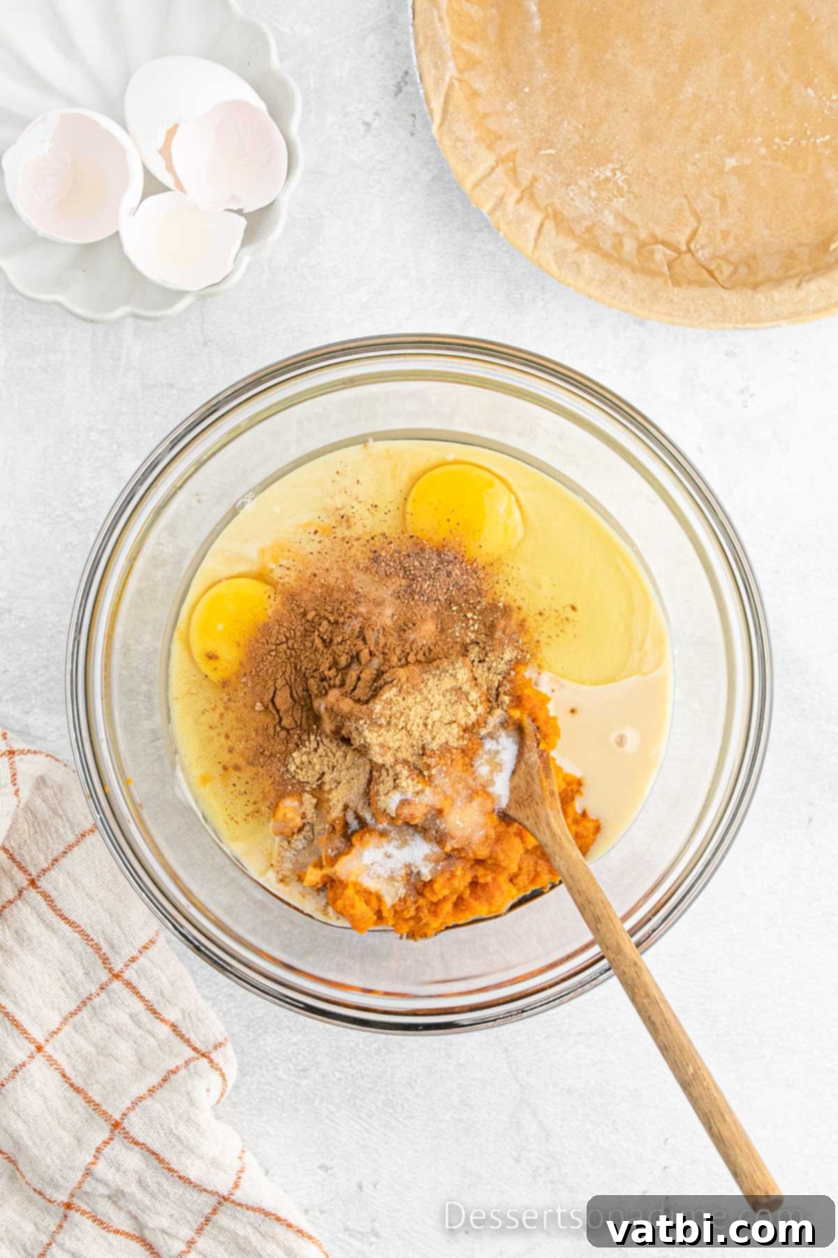 A medium bowl filled with combined pumpkin pie ingredients, featuring a smooth, creamy texture and a rich orange color, indicating readiness for baking.