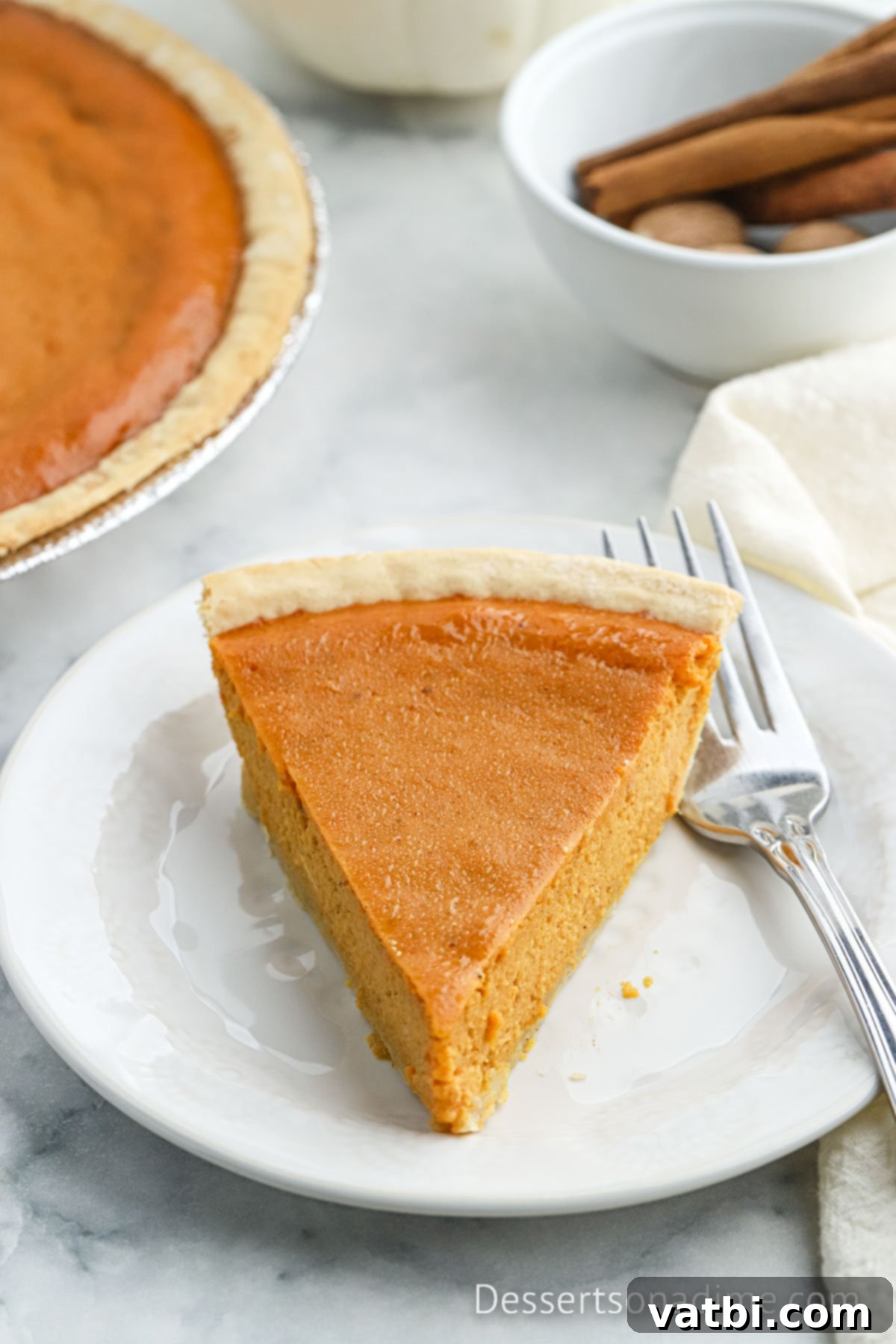 A tempting slice of Eagle Brand Pumpkin Pie, topped with a swirl of whipped cream, presented on a white plate, highlighting its smooth texture and festive appeal.
