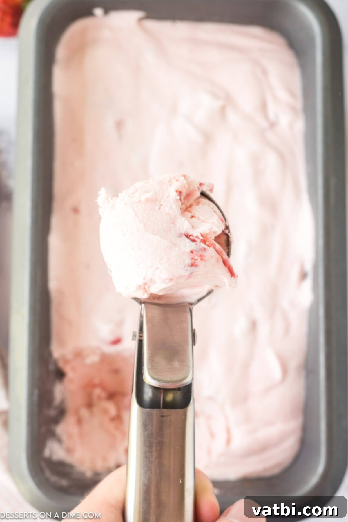 Easy No-Churn Strawberry Ice Cream 10 A scoop of no-churn strawberry ice cream being taken from the loaf pan after freezing, showing its creamy texture.