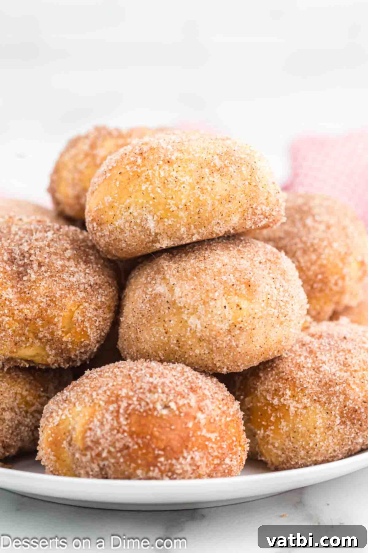 Air-Fried Apple Pie Puffs 12 A stack of perfectly golden Air Fryer Apple Pie Bombs, coated in cinnamon sugar, on a white plate.