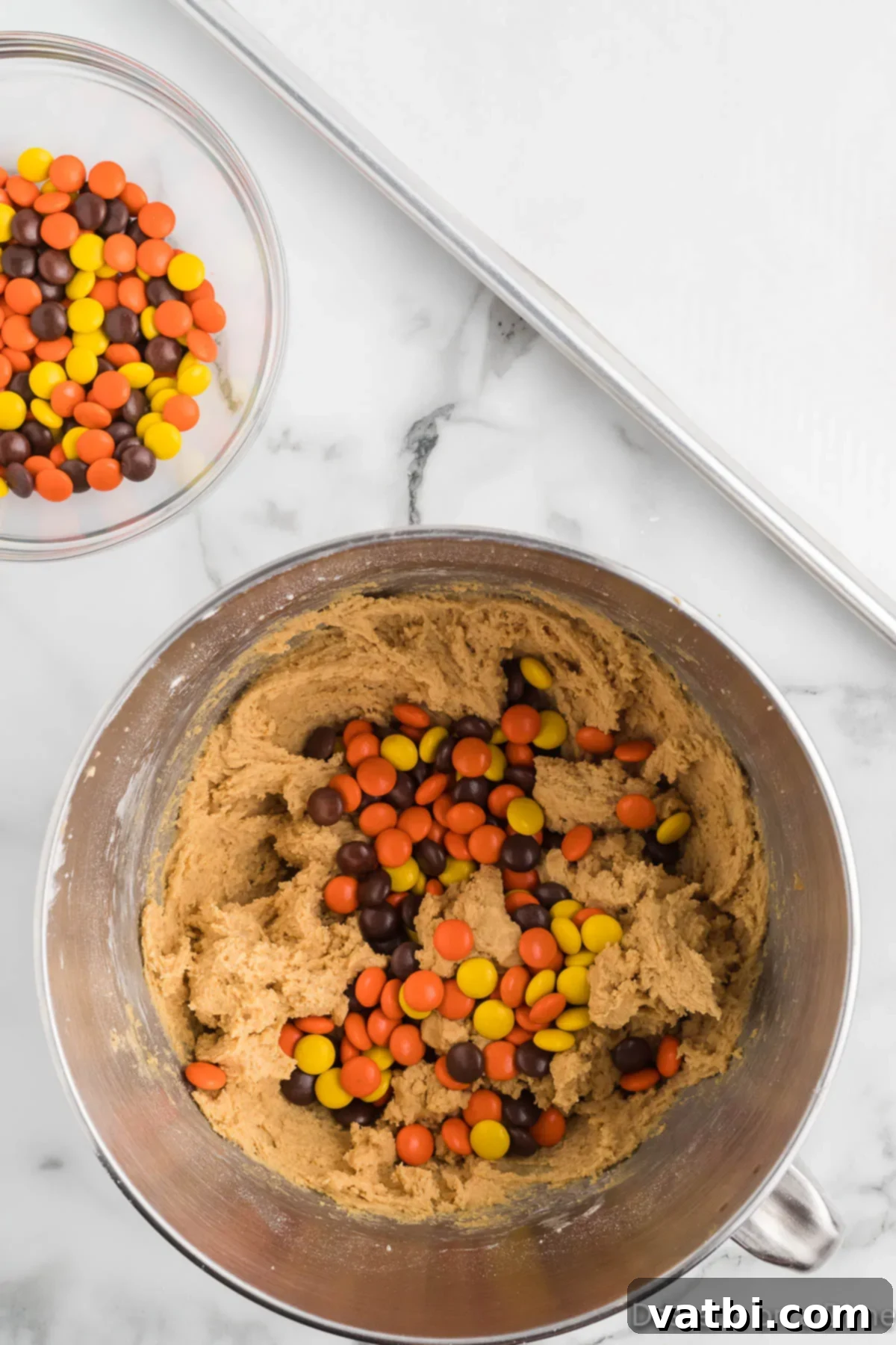 Reese's Pieces Peanut Butter Perfection 8 Reese's Pieces candy being gently folded into cookie dough with a spatula.