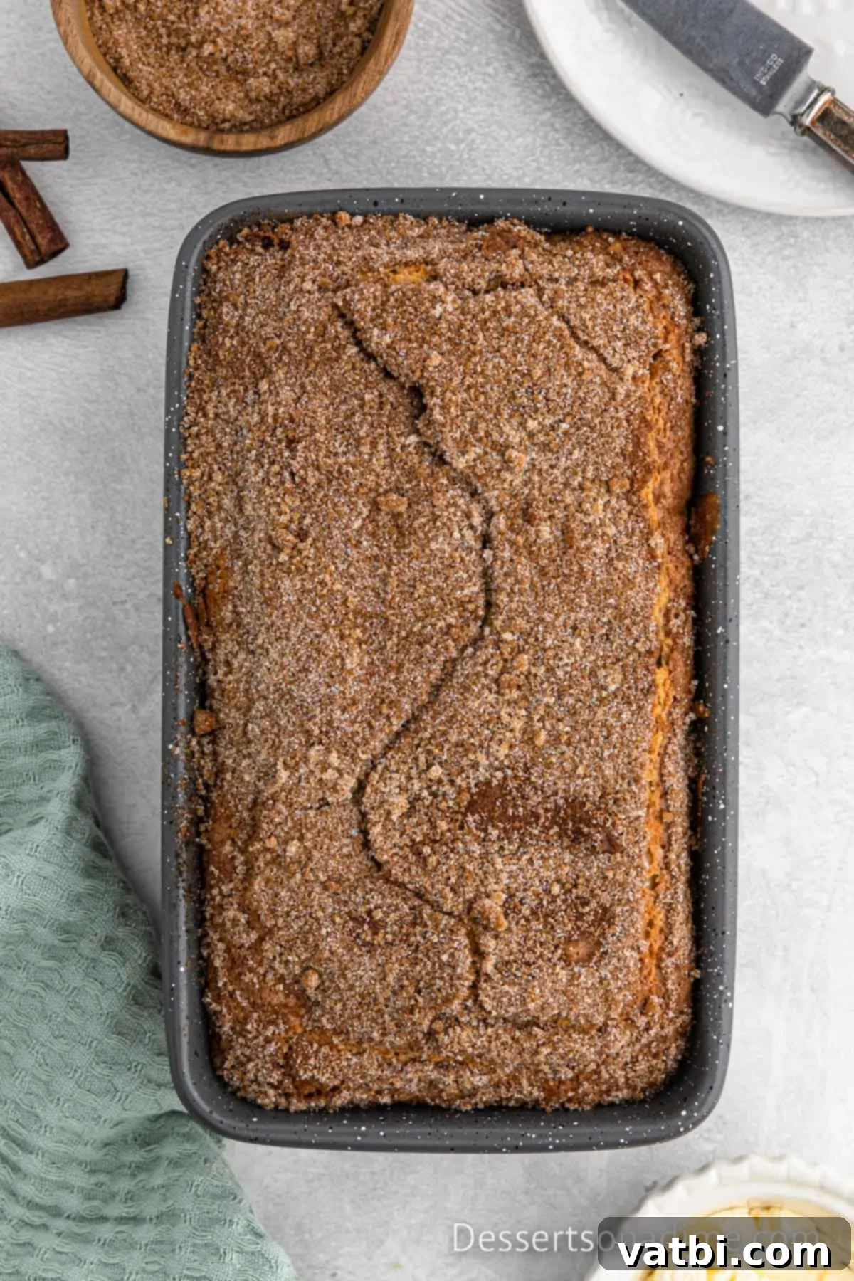 Cinnamon Sugar Snickerdoodle Bread 10 Baked Snickerdoodle Bread still in the loaf pan, showing a cracked cinnamon sugar topping.