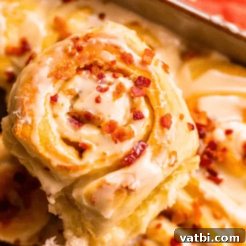 Close-up of Maple and Bacon Cinnamon Rolls with generous frosting and bacon topping.