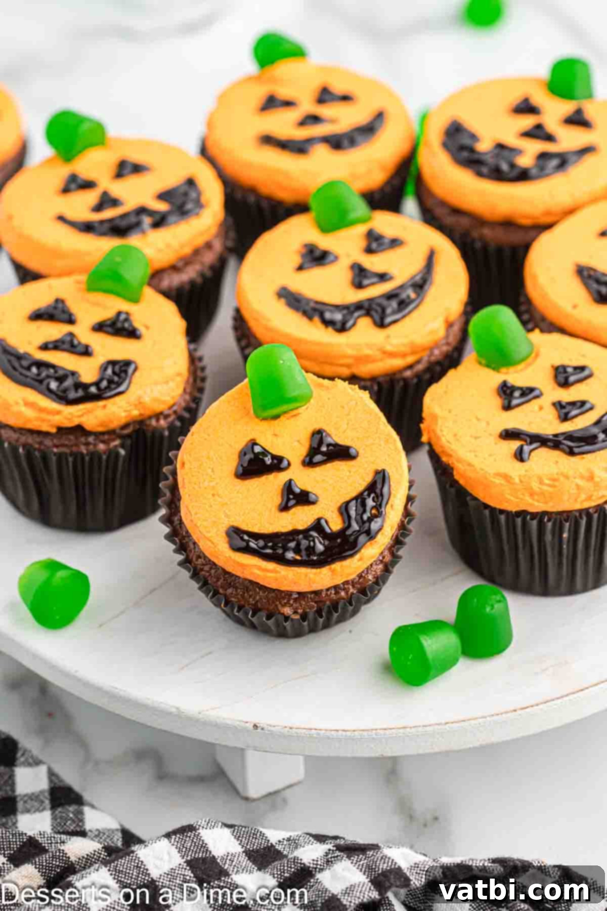 Carved Pumpkin Cupcakes 2 Close-up of festive Jack-O-Lantern Cupcakes displayed on a cake stand, ready for a Halloween party.