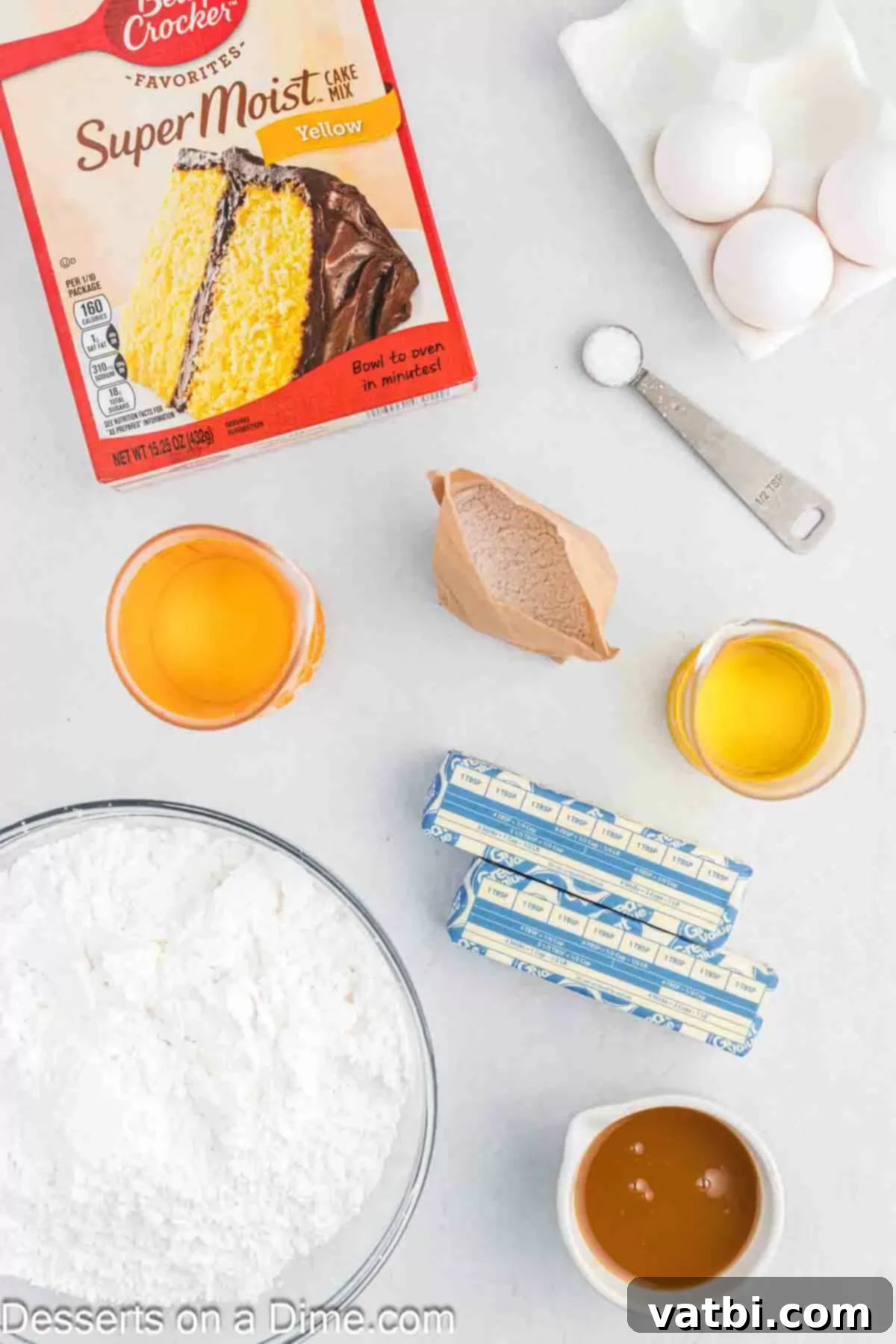 Display of main ingredients for butterscotch cupcakes and frosting: a box of yellow cake mix, butterscotch pudding mix, bottle of vegetable oil, raw eggs, bag of powdered sugar, salt shaker, and a jar of butterscotch sauce.