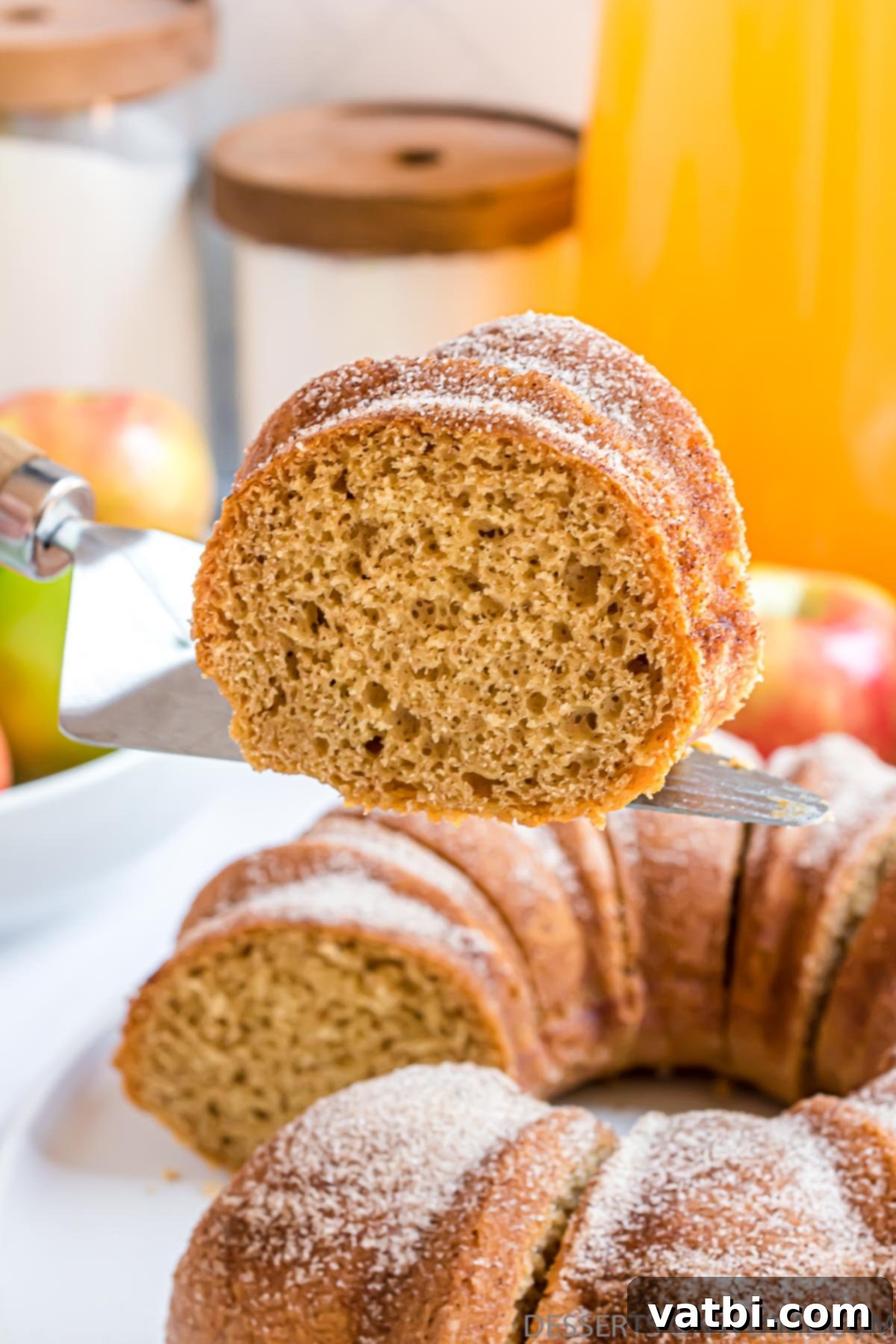 Harvest Apple Cider Bundt 2 A slice of golden brown Apple Cider Bundt Cake, showcasing its moist interior and generous cinnamon sugar coating, ready to be served on a white plate.