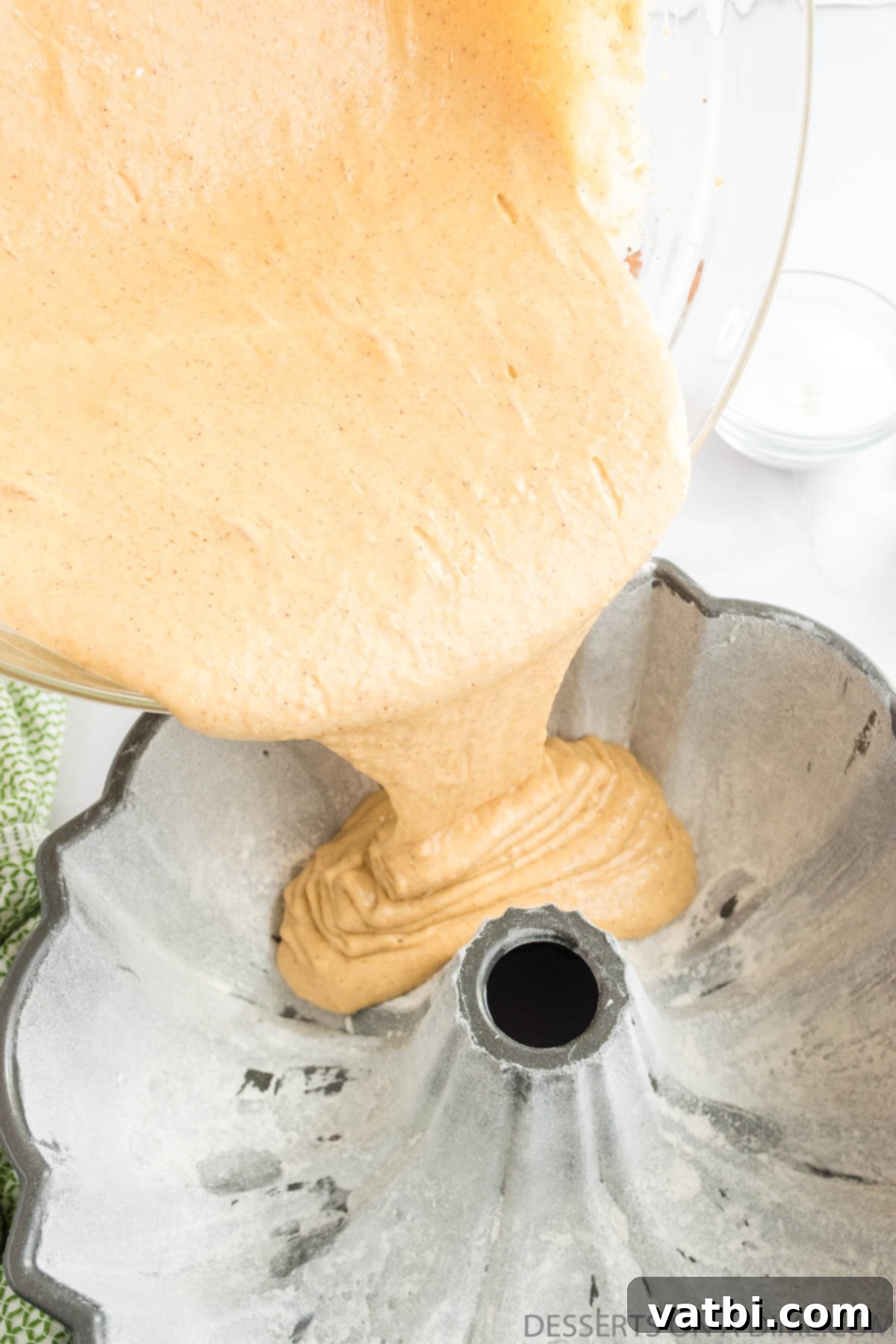 Harvest Apple Cider Bundt 6 Thick, golden cake batter being carefully poured from a mixing bowl into a prepared bundt pan.