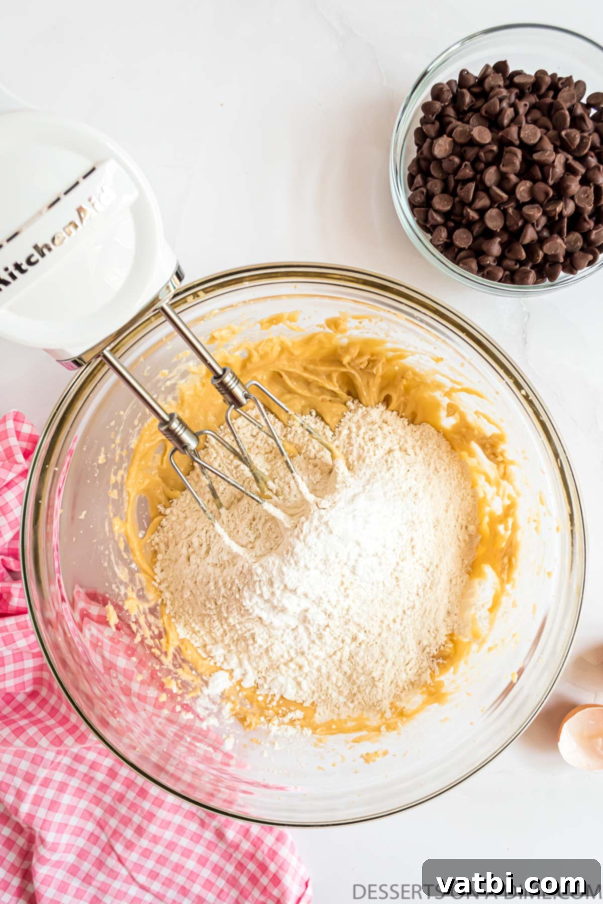 Decadent Cream Cheese Chocolate Chip Cookies 6 Dry ingredients including flour, cornstarch, baking soda, and salt being gradually mixed into wet ingredients to form cookie dough.