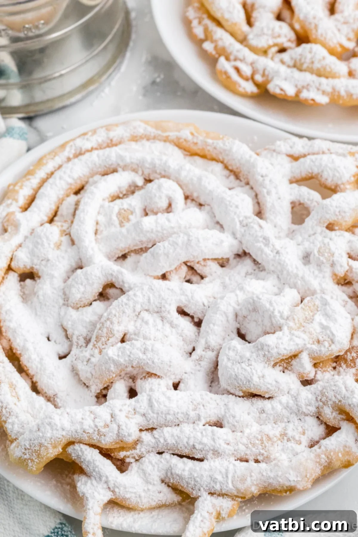 Sweet Funnel Cake Perfection 11 A single funnel cake topped liberally with powdered sugar on a white plate.