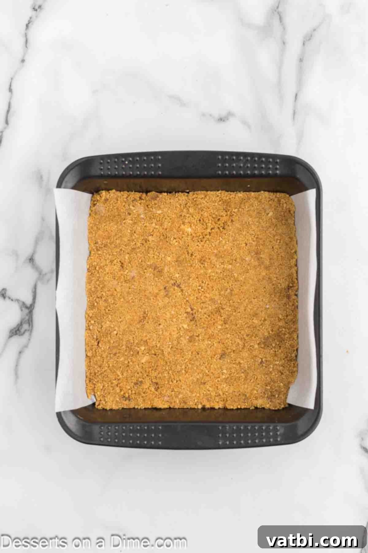 Graham cracker crumbs firmly pressed into an 8x8 inch baking dish, ready for baking.