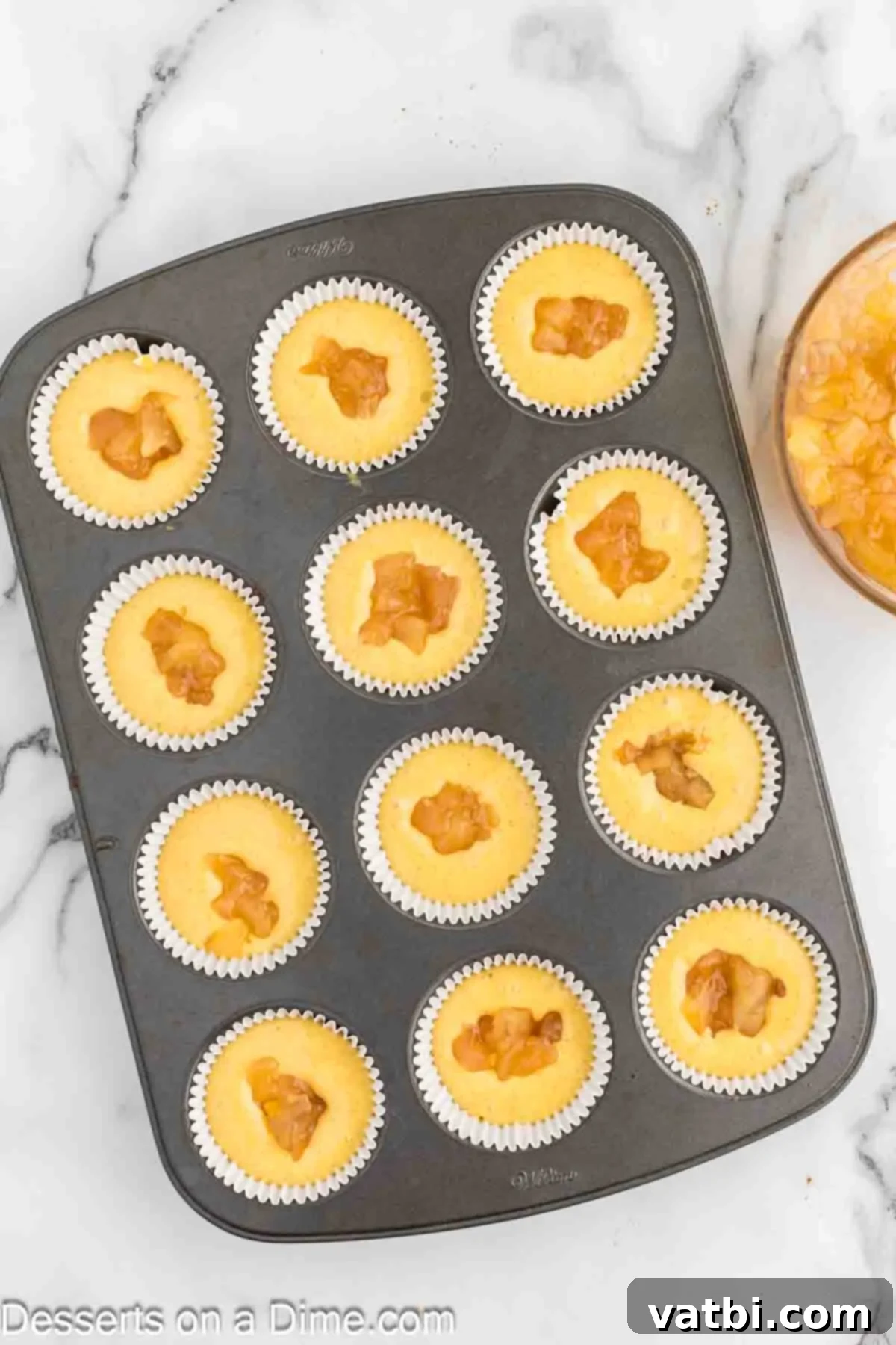 Apple Crumble Cupcakes 5 Cupcake liners filled with batter, each topped with a spoonful of apple pie filling.