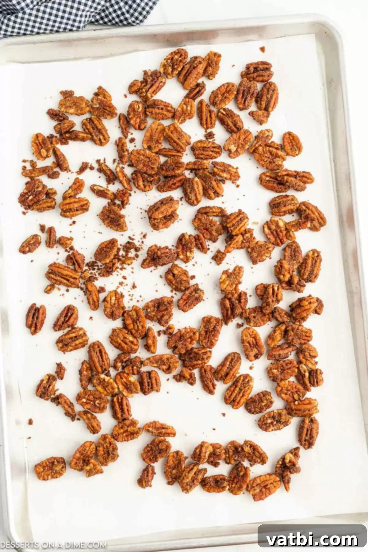 Freshly air-fried candied pecans spread out on a baking sheet lined with parchment paper, cooling.